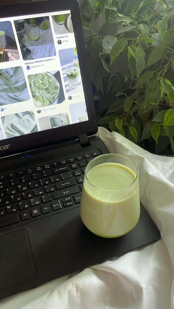 pexels photo 12266706 12266706 Glass of green milk drink on laptop keyboard amidst lush indoor plants.